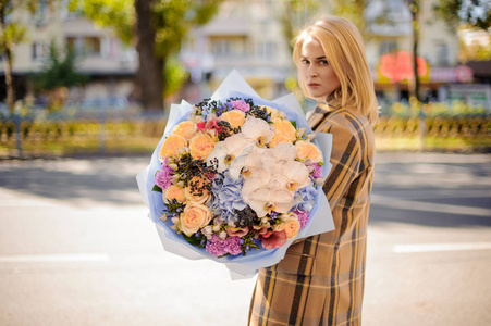 金发女子在格子大衣举行了一个可爱的大花束的花朵对城市在秋季日