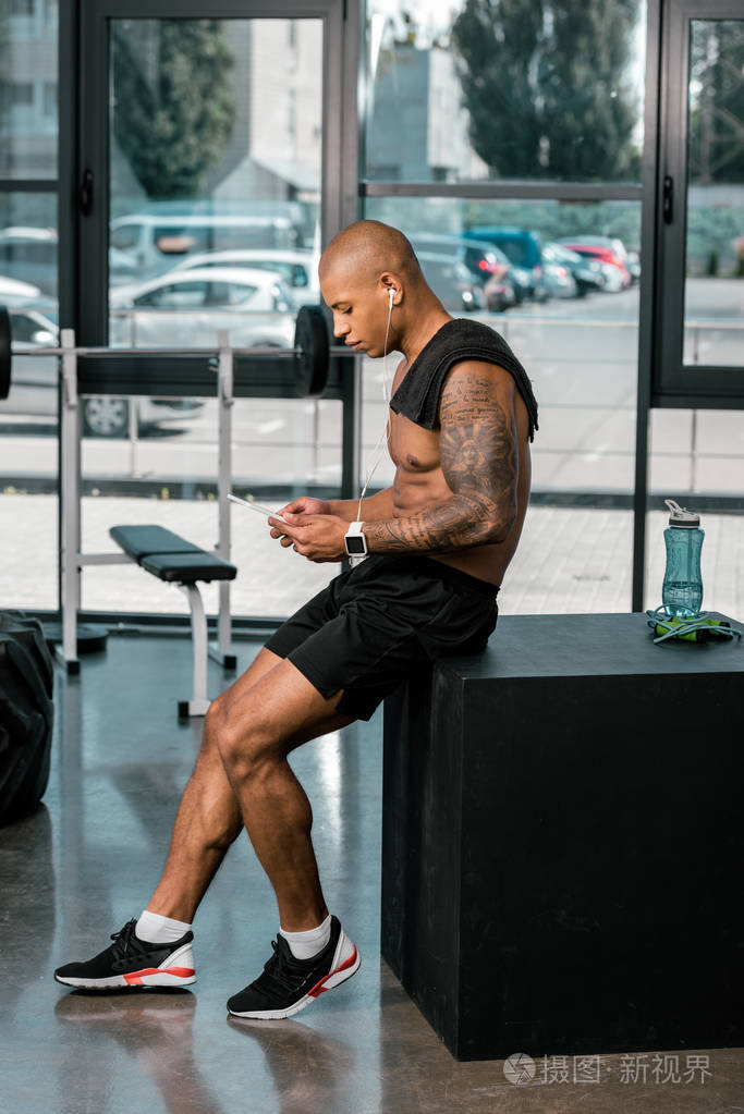 肌肉年轻纹身非洲裔美国运动员的侧面视图在健身房使用数字平板电脑