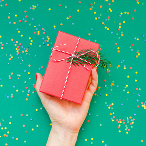 新年或圣诞顶级景观圣诞假期庆祝妇女手红色指甲持有礼物盒复制空间绿色纸张背景。模板贺卡