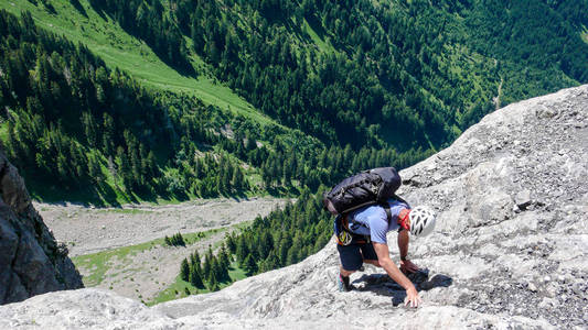 登山者在陡峭的岩石和卵石斜坡上, 他的方式与绿色山谷下面的山顶