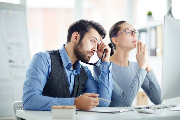 两名办公室经理坐在电脑显示器前, 等待在线页面加载