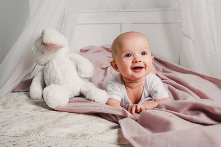 一个小婴儿躺在床上, 玩具兔子和微笑