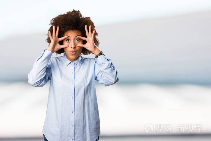 年轻的黑女人做睁开眼睛手势在模糊的背景