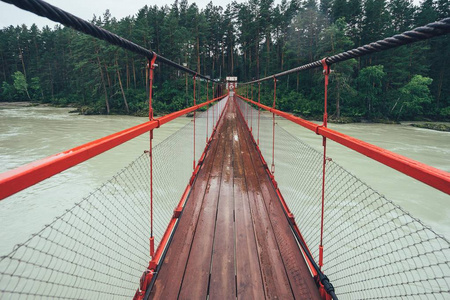 在河上的吊桥。下雨的天气, 在河上的桥上的森林的道路