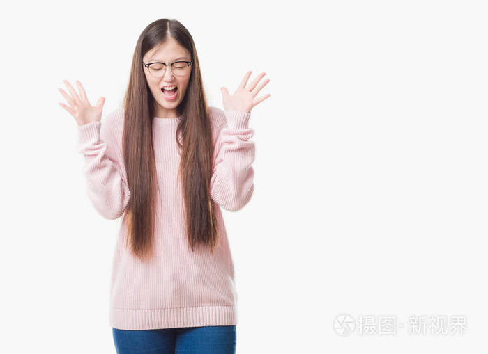 年轻的中国妇女在孤立的背景戴眼镜庆祝疯狂和疯狂的成功与手臂举起和闭上眼睛尖叫兴奋。赢家理念