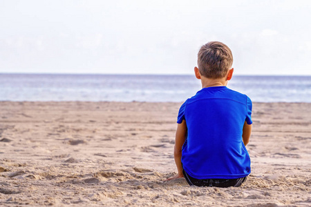 悲伤孤独的孩子坐在海滩上, 看着大海, 思考