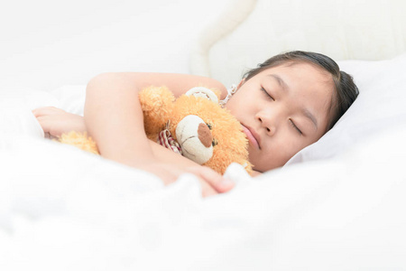 可爱的小亚洲女孩睡觉和拥抱在床上的玩具熊