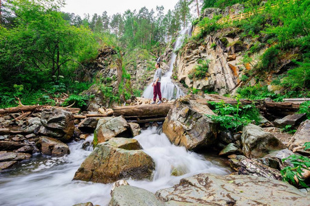 一个女孩站在一个瀑布附近的原木上。森林中的山瀑布