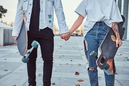 年轻时髦的穿着溜冰者的裁剪照片在靠近摩天大楼的时候手牵着手