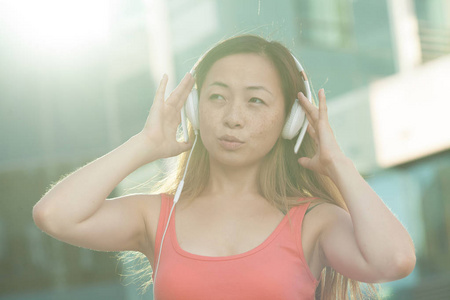 亚洲女人快乐地微笑着, 在现代城市里用电话听音乐