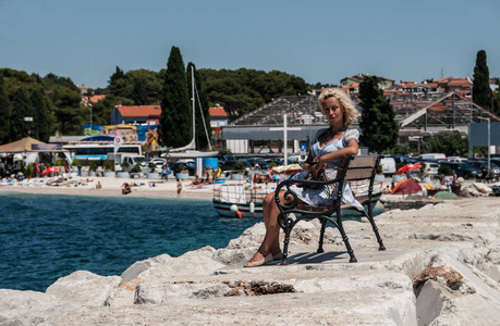 一个年轻的欧洲金发女郎坐在靠近地中海的长凳上。