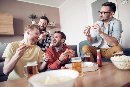 四男性朋友在家里看电视, 同时吃比萨饼和喝啤酒