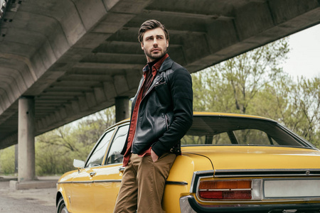 沉思时尚男子在皮革夹克站在老式汽车和看着远离