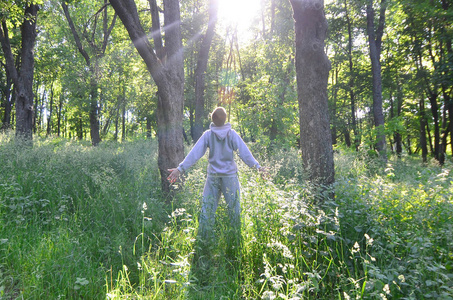 一个穿着灰色运动服的年轻人在森林里的树上晒太阳.
