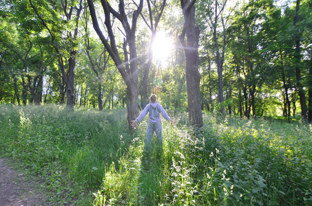 一个穿着灰色运动服的年轻人在森林里的树上晒太阳。娱乐期间在露天森林的体育奔跑。美丽黎明的喜悦