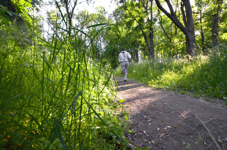 一个穿着灰色运动服的年轻人沿着树林里的树林走来走去。户外运动慢跑