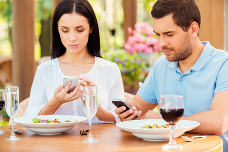 在餐厅，在智能手机上键入对年轻的夫妇