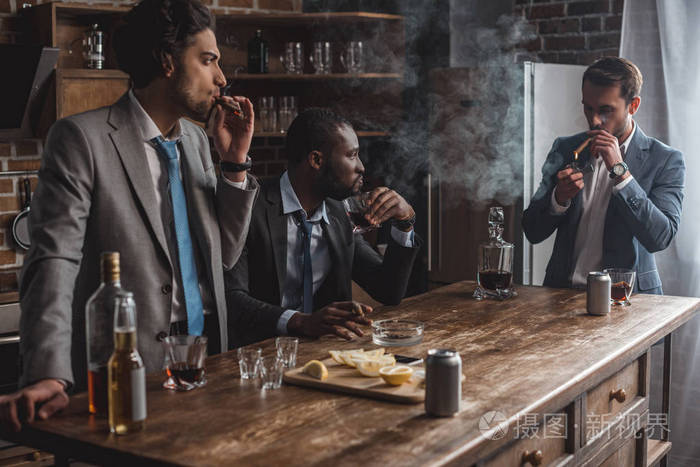 年轻的多民族商人在聚会时抽雪茄和饮酒