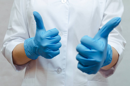 护士在医疗礼服和在手上的医疗手套显示竖起大拇指的手势。良好的治疗效果