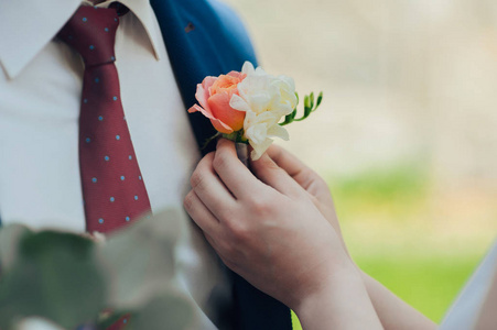 新娘的手放在新郎夹克上的胸花花上。