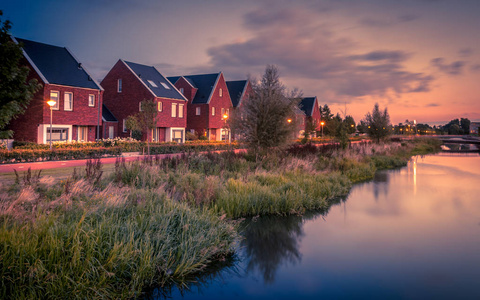 在荷兰 Veenendaal 市, 拥有生态友好河岸的现代生态中产阶级家庭住宅, 街道上长时间曝光的夜拍。复古外观图像