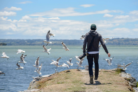 年轻男性摄影师追逐群海鸥鸟在湖附近照片