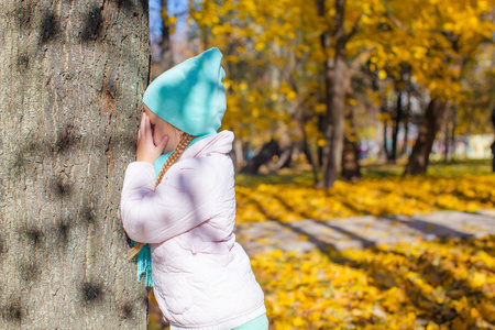 小女孩在玩捉迷藏的游戏树在秋天公园附近