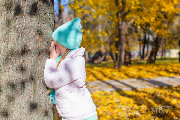 小女孩在玩捉迷藏的游戏树在秋天公园附近