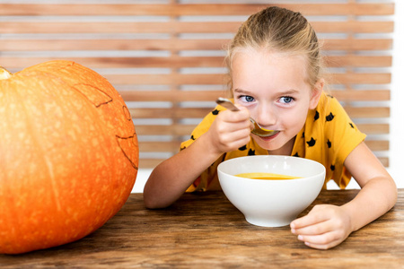 可爱的小女孩吃南瓜汤。万圣节概念背景