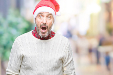 中年老人戴着圣诞节帽子在孤立的背景害怕和震惊的惊讶的表情, 恐惧和兴奋的脸