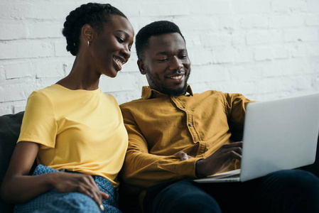 快乐年轻的非洲裔美国人夫妇使用笔记本电脑一起在家里