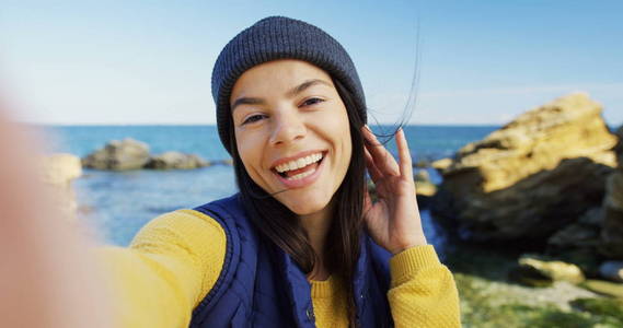 迷人的黑发女人在岩石的海边做漂亮的 selfies。寒冷晴朗的天气。户外.pov.关门了肖像