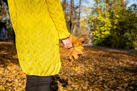 穿着黄色夹克的女人手中握着五颜六色的叶子