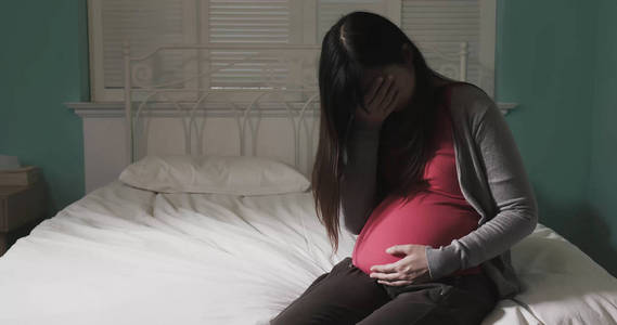 怀孕的妇女坐在床上感到抑郁在家中