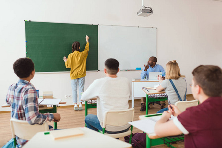 学生在粉笔板上的背观与教师坐在教室里的同学