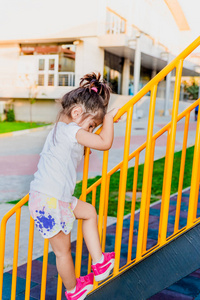 可爱的小女孩从操场上的金属楼梯杆爬的背面视图