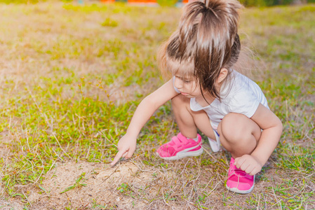 可爱的小女孩的肖像触摸小蚂蚁与她的手指在蚂蚁山上的土壤地面