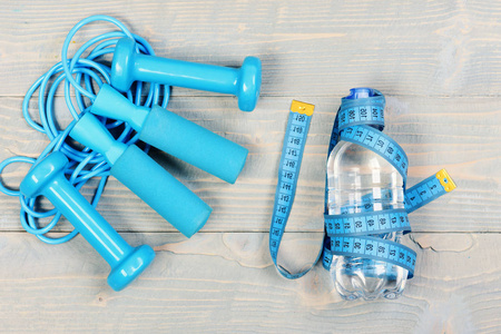 厘米在青蓝色被栓在瓶在木古董背景。健康和积极的生活方式的工具。哑铃, 测量胶带和跳绳, 顶部视图。锻炼和减肥概念