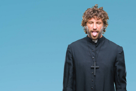 英俊的西班牙天主教神父男子在孤立的背景下坚持舌头出来快乐与滑稽的表达。情感概念