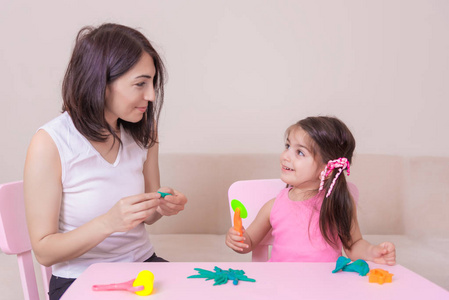 美丽的母亲和可爱的女孩一起玩 playdough, 而坐在桌上