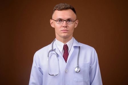 戴眼镜的年轻男子医生对棕色背景