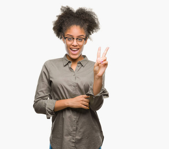 年轻的美国黑人妇女戴着眼镜在孤立的背景微笑着快乐的脸眨眼在相机做胜利标志。第二个