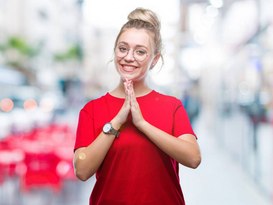 年轻的金发女人戴着眼镜在孤立的背景祈祷双手一起请求原谅微笑自信