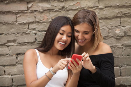 两个快乐的女人朋友共享社会媒体在户外在公园里的智能手机