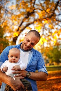 秋天公园里年轻的微笑的父亲和男婴肖像