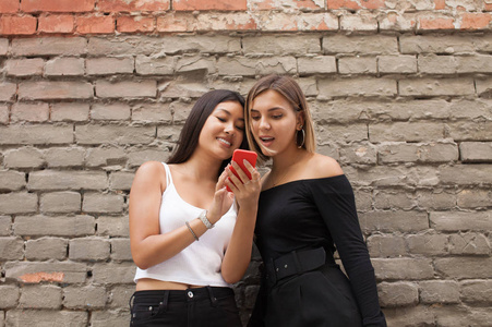 两个快乐的女人朋友共享社会媒体在户外在公园里的智能手机