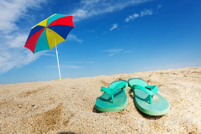 热带背景与翻转的拖鞋和太阳伞在沙滩上