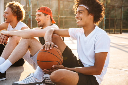年轻职业篮球运动员的照片坐在操场上户外和观看比赛在夏季晴朗的一天