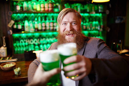 兴奋胡子的男子与玻璃泡沫啤酒无比与他的朋友在酒吧