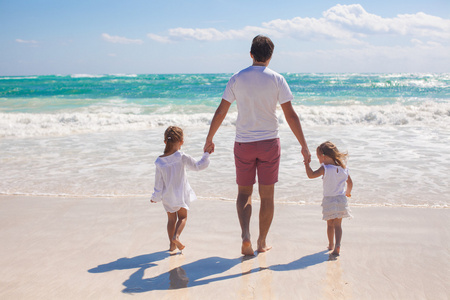 父亲和两个可爱女儿白砂沙滩上散步的后视图
